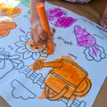 Kid coloring with orange crayon on a mat that shows garden elements