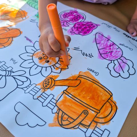 Kid coloring with orange crayon on a mat that shows garden elements