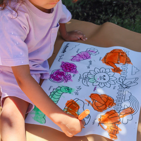 Kid coloring while sitting on floor, using orange crayon and mat feastures garden elements