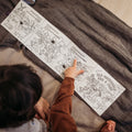 A child sits on a bed pointing at a colorful HeyDoodle silicone coloring book, with another closed silicone book nearby.