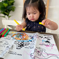 Little girl holding yellow crayon, coloring on mat that shows mama animals and the little baby animals