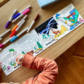 A child colors a HeyDoodle silicone reusable coloring mat, filled with vibrant animals and nature scenes, using colorful markers.
