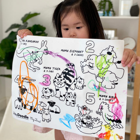 Little girl holding mat that features mama animals and her baby animals, random colours drawn on the mat mat shows kangaroo, elephant, tiger, sheep and birds